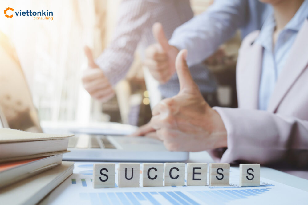 Khái niệm thành công trong teamwork kinh doanh với mọi người giơ ngón tay cái lên phía sau các khối gỗ đánh vần từ SUCCESS trên bàn làm việc